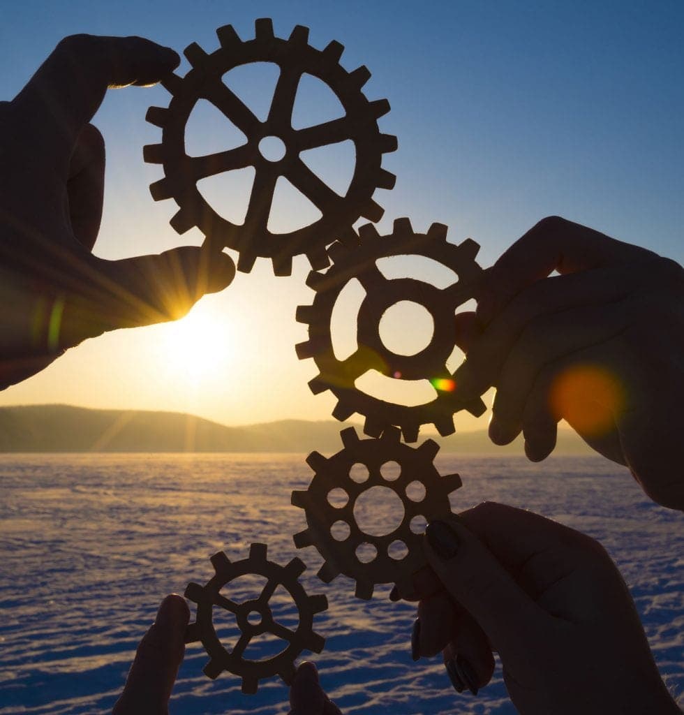 four hands holding gears against the setting sun
